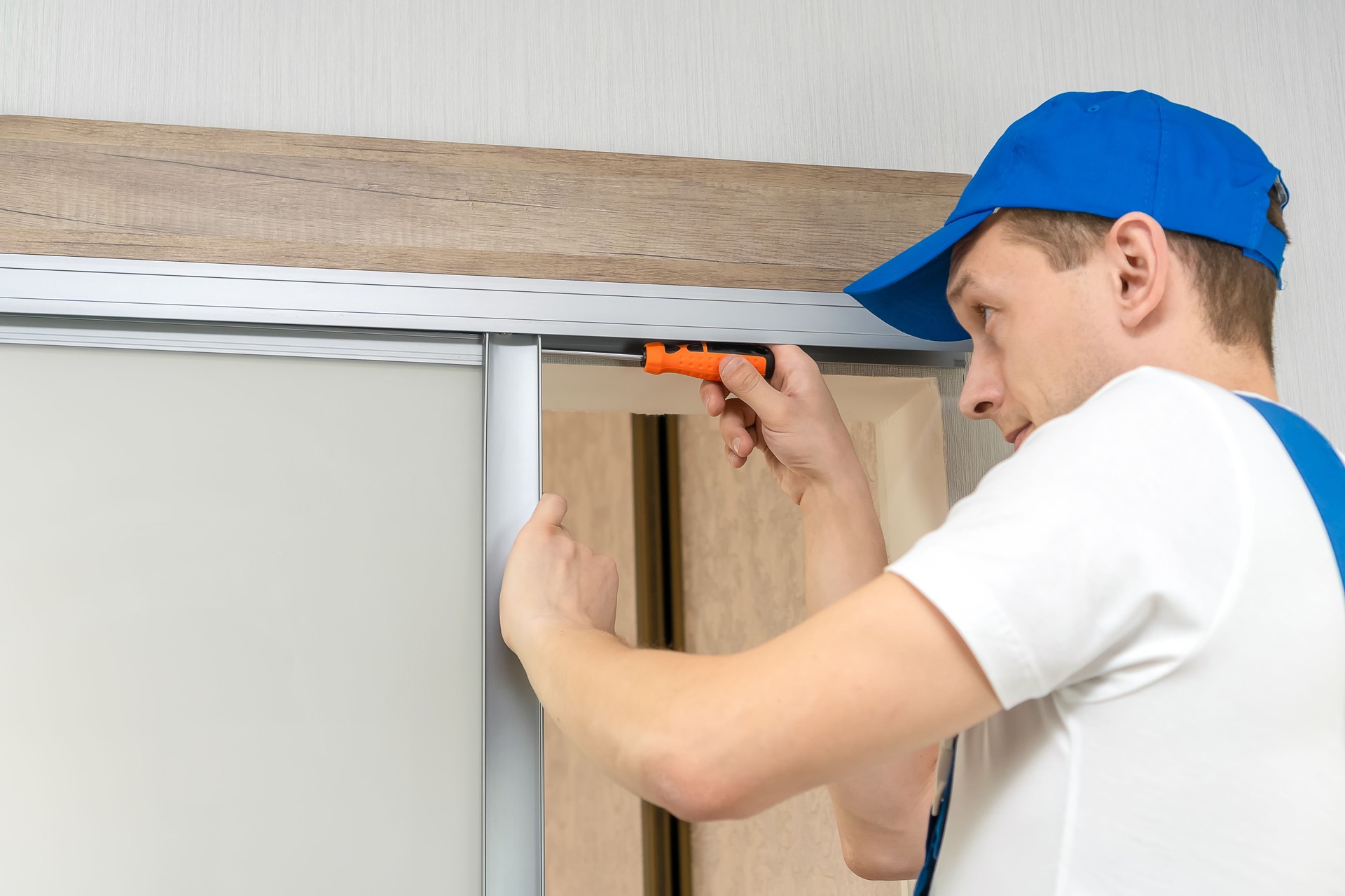 Handyman who installs sliding doors at home in overalls with a screwdriver in his hands repairs the door